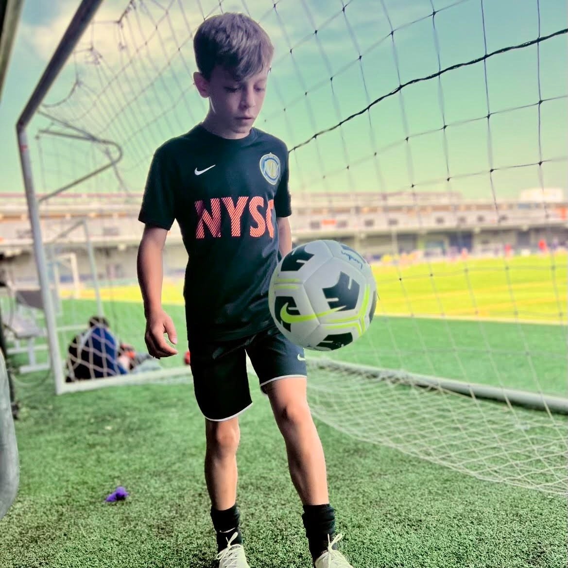 Young boy balancing a soccer ball on his knee in front of a goal